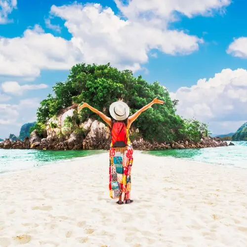 Happy traveler raising arms on island beach, showcasing travel money tips UAE for budget-friendly vacations